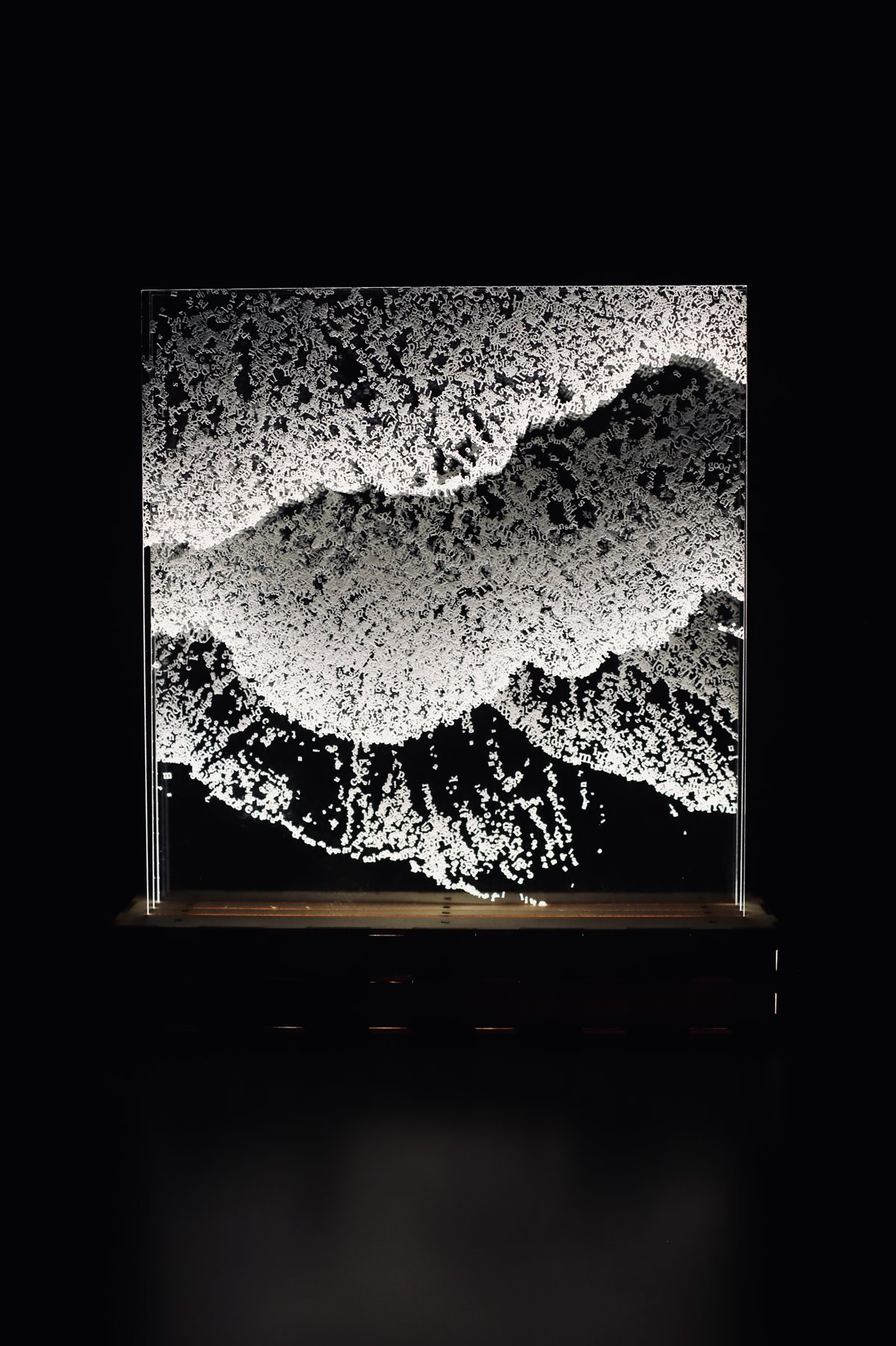 Front view of illuminated transparent panels, with layered letters forming waves against black.