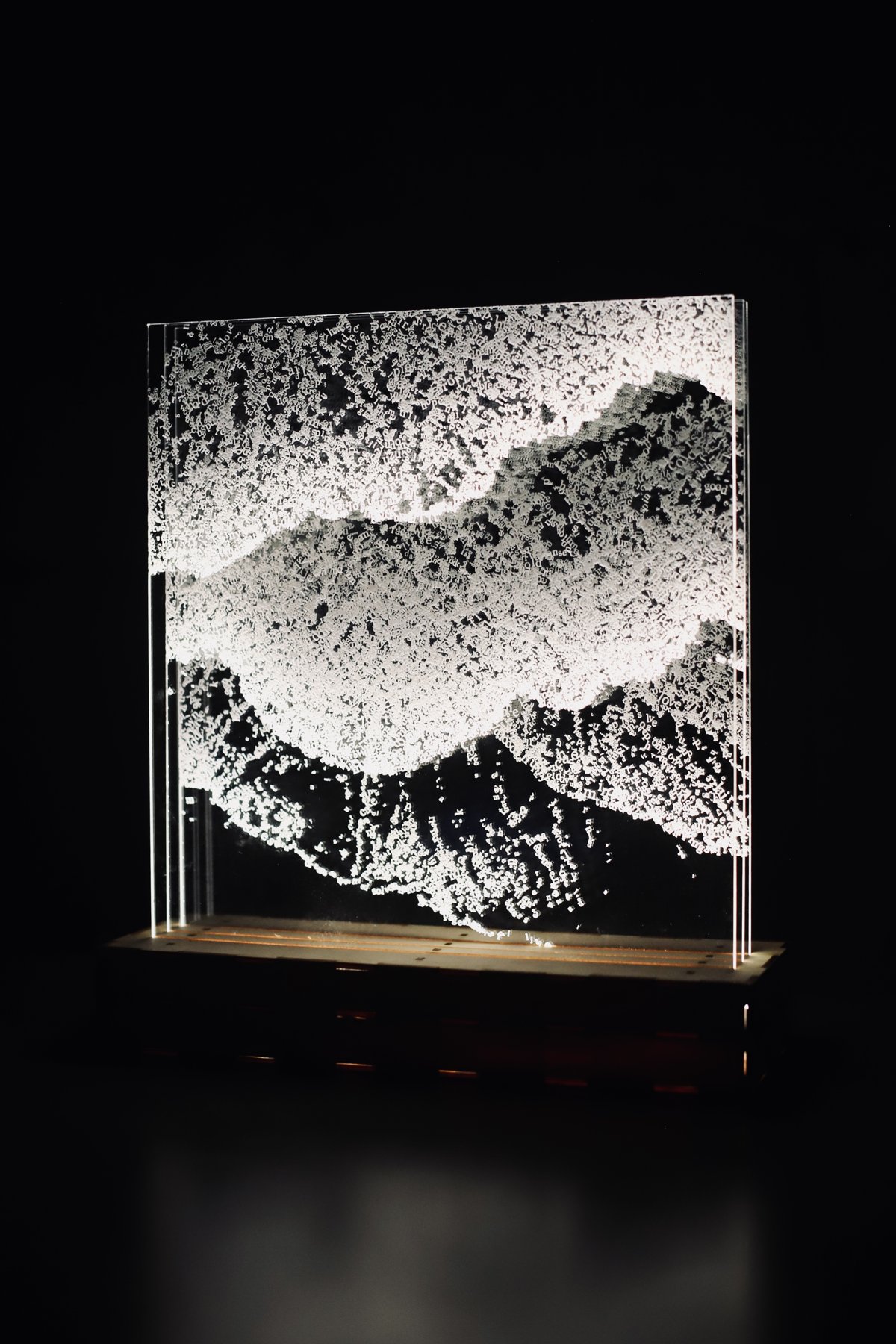 Three-quarter view of the illuminated text waves and their wooden base.