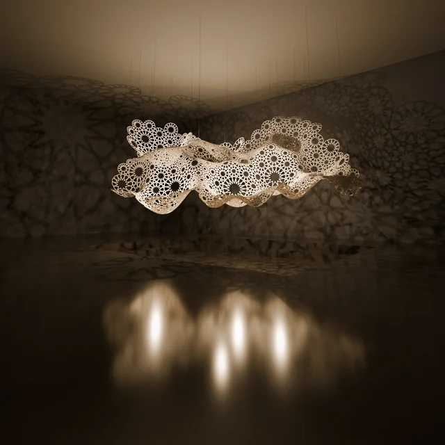 Suspended rosette-patterned sculpture casting shadows across a warmly lit room and reflective floor