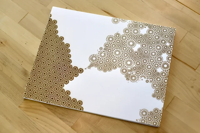 Yearning (for a Fantasy): rosette patterns engraved on white paper resting on a wooden floor