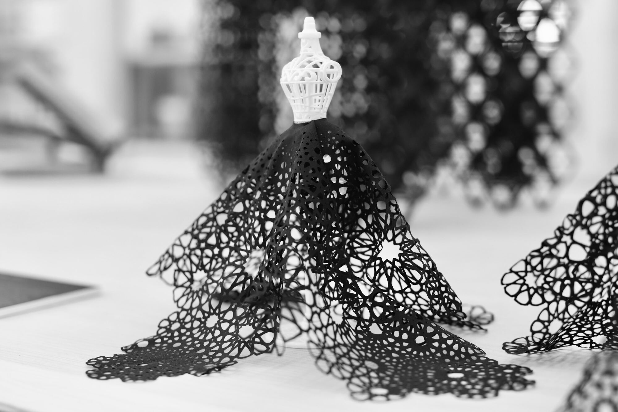Close installation view of a black cutwork textile sculpture on a miniature dress form at Polymaths